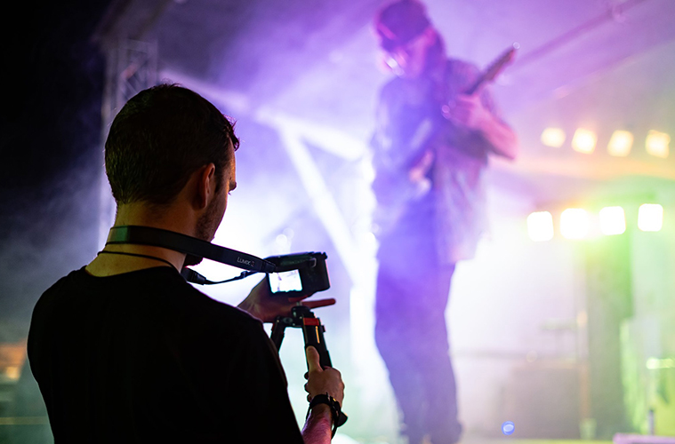 Videographer Standing in front of the stage with lights flashing and a guitarist playing a solo