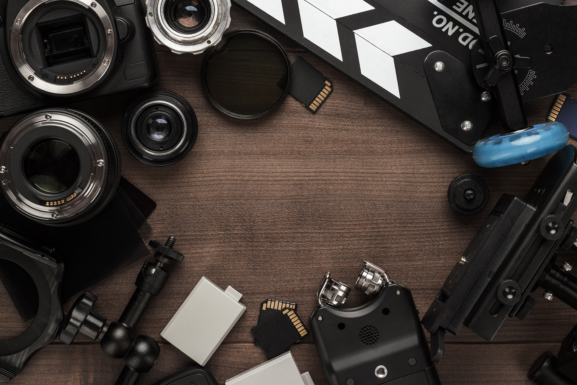 Assorted digital cameras, lenses, sd cards, camera batteries and video equipment assorted on a wooden table